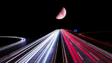 Streaks of light from cars on a highway with the moon and stars in the background