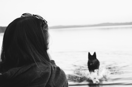 The girl on the beach looks at the dog. Sad black and white photo.の写真素材