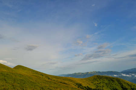 Cloudy blue sky upon green mountainsの写真素材