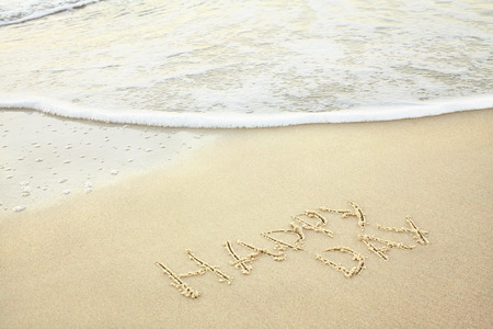 handwritten inscription happy day made in the sand near the water, the wave washes text on the beachの写真素材