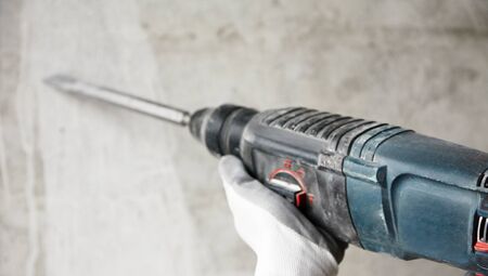 Abstraction photo of noisy repair. electric tool in the hands of a construction worker, gadder against a concrete wall, old worn rock-drillの写真素材