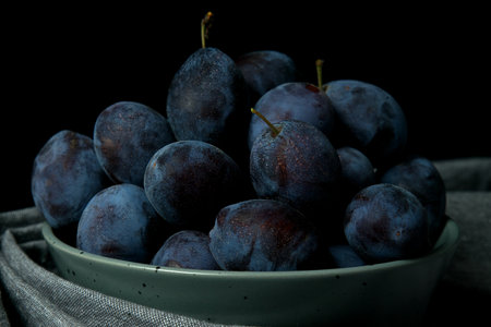 Ripe purple plums in a bowl on a black background. Selective focus. Toned.の写真素材