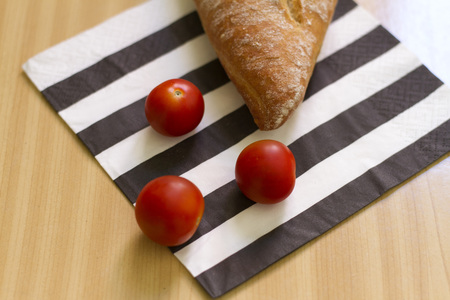 Loaf of bread and cherry tomatoes on a black and white striped napkinの写真素材