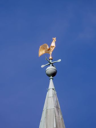 weather vane as a gold cock on the high cone roof of old buildingの写真素材