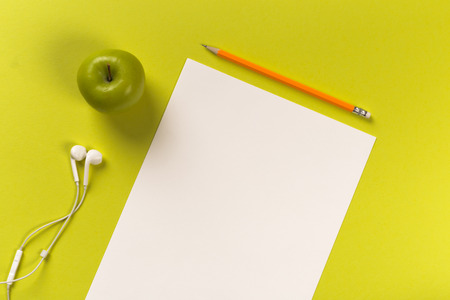 Pencils with white paper sheets on coloured backgroung, Office tool, white headphones and green appleの写真素材