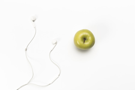 single green color apple and digital audio headphones isolated on white backgroundの写真素材