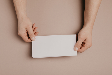 Man holds a mock-up letter or postcard in his hands with envelope on a brown backgroundの写真素材