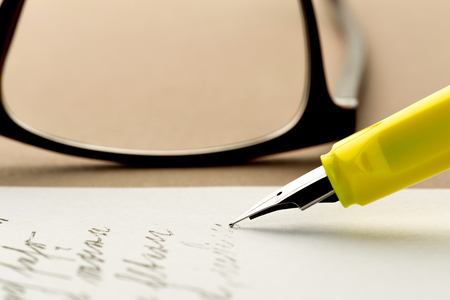 yellow fountain pen writing a letter, glasses behindの写真素材