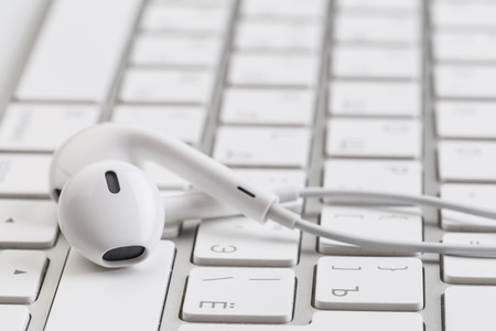 white earphones on white keyboardの写真素材