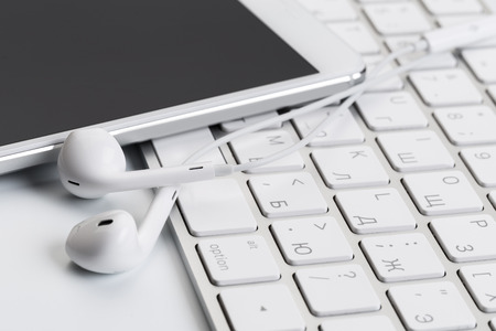white earphones on white keyboard with phone