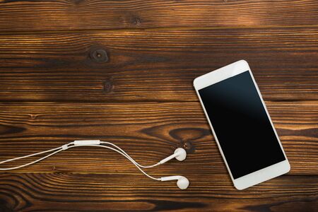 white smartphone with headphones on wooden background- Image