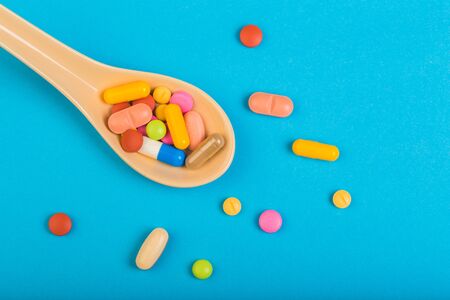 Colorful medical pills on spoon and capsules or supplements for therapy in background, concept of...