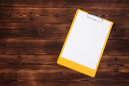 Clipboard with white sheet on wood background. Top view. - Image
