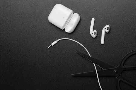 Air Pods. with Wireless Charging Case. New Airpods 2019 on dark  background. Airpods. female headphones. Scissors cut the cable 3.5 headphonesの写真素材
