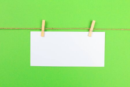 a piece of white paper attached to a rope clothespin on green background の写真素材