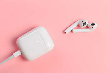 White headphones with box case on pink background. Modern technology pods with air connection. Wireless earphones device. New way to leasten music. Concept of free choice.のeditorial素材