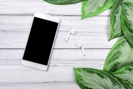 tropical leaves  and smartphone with earphones on white wooden background with text place    - Image