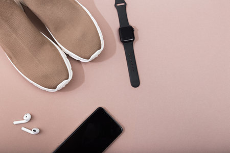 modern beige sneakers with phone, smart watch and earplugs on beige background