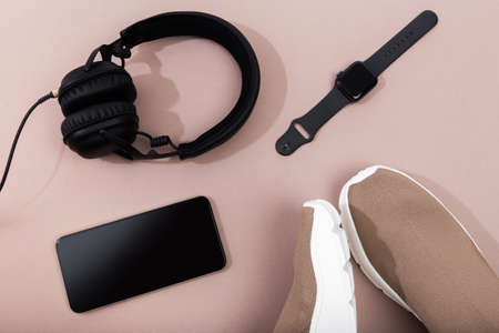 modern beige sneakers with phone, smart watch and earplugs on beige backgroundの写真素材