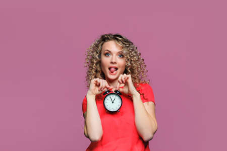beautiful young woman   with curl hair  posing  on pink   background  with clockの写真素材