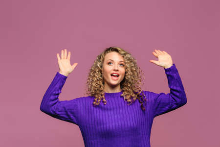 beautiful young woman   with curl hair in knitted violet sweater posing   on pink   backgroundの写真素材