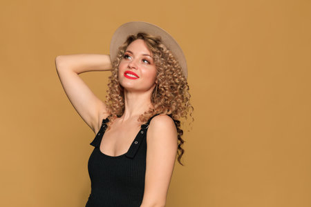 beautiful young woman    with curl hair and hat posing  on beige  backgroundの写真素材