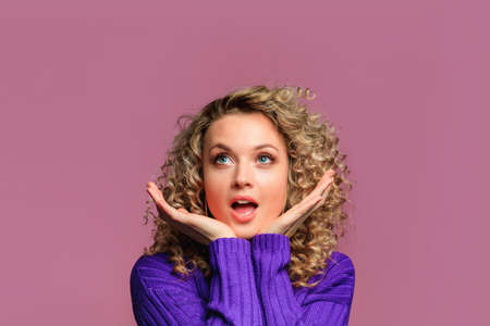 beautiful young woman   with curl hair in knitted violet sweater posing   on pink   backgroundの写真素材
