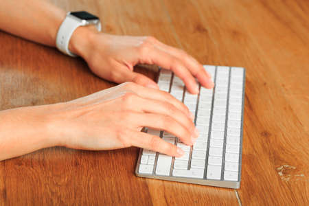 Female hands typing on white wireless modern keyboard  on wooden table