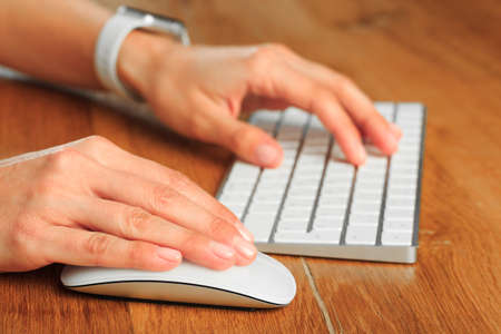 Female hands typing on white wireless modern keyboard  on wooden table
