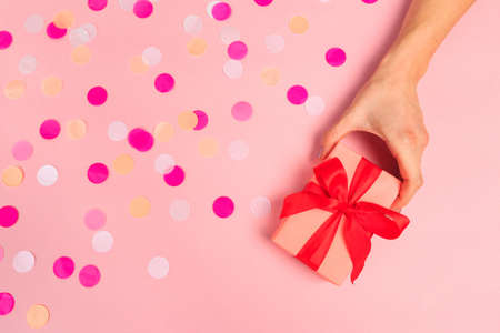Woman presenting gift box top view on pastel pink background with pink confetti. Giving presents...