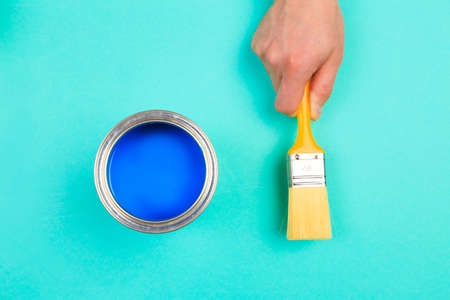 hand holding Brush  on open can of blue  paint on pastel blue  background. Renovation conceptの写真素材