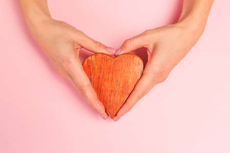 Beautiful young woman's hands holding  wooden  heart on pastel pink background - Imageの写真素材