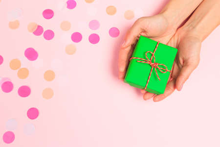 Woman presenting gift box top view on pastel pink background with pink confetti. Giving presents concept, card for Mother's Day, Women's Day or any other holiday or celebrationの写真素材