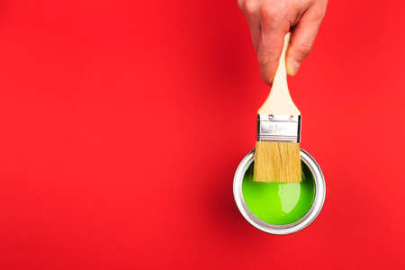 hand holding Brush  on open can of   paint on red  background. Renovation conceptの写真素材