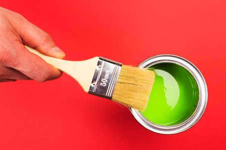 hand holding Brush  on open can of   paint on red  background. Renovation conceptの写真素材