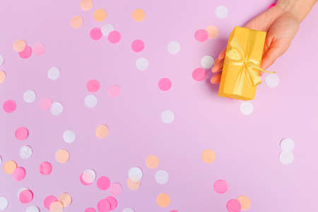 Woman presenting gift box top view on pastel pink background with pink confetti. Giving presents concept, card for Mother's Day, Women's Day or any other holiday or celebrationの写真素材