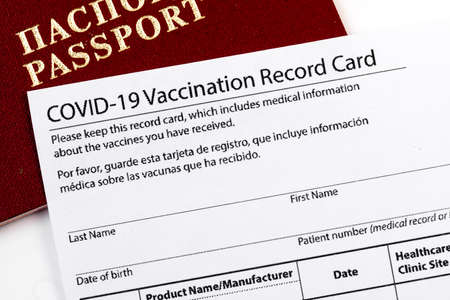 Coronavirus vaccination record card, biometric passport and blue medical mask on light gray desk....