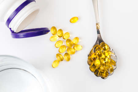 Close up of  oil filled capsules suitable for: fish oil, omega 3, omega 6, omega 9,  vitamin A, vitamin D, vitamin D3, vitamin E with white bottle and spoonの写真素材