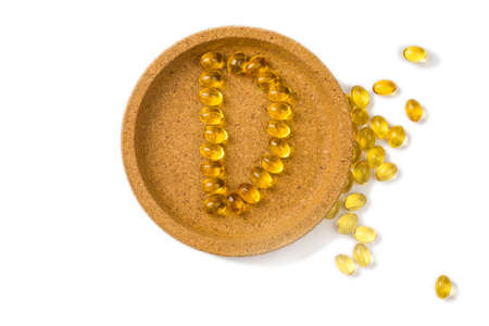 Yellow oil capsules with vitamin D3forming shape D on the white background.の写真素材