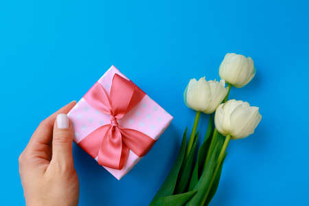 Womans hand holding Gift box .Spring flowers on color background. Happy women's day. Happy Mothers day.Hello Springの写真素材