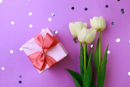 Gift box and spring flowers with confetti on color background. Stylish soft image of spring flowers....