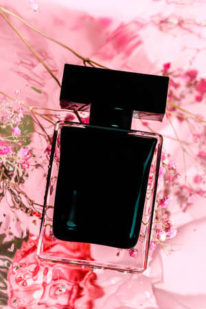 Full jar of perfume on pink background with water and flowers