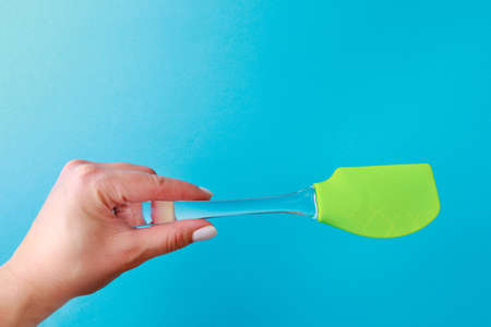 Womans hand holding silicone green spatula with plastic handle on color backgroundの写真素材