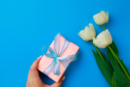 Womans hand holding Gift box .Spring flowers on color background. Happy womens day. Happy Mothers day.Hello Springの写真素材