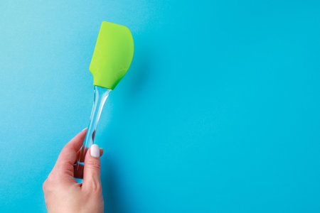 Womans hand holding  silicone green spatula with plastic handle on color backgroundの写真素材
