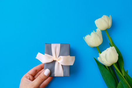 Womans hand holding Gift box .Spring flowers on color background. Happy womens day. Happy Mothers day.Hello Springの写真素材
