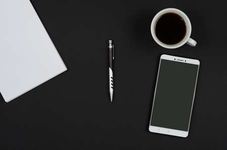 Notebook, coffee and smartphone on black desk.の写真素材