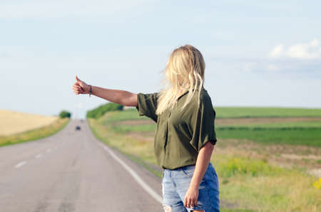 Blonde holding sign while hitchhiking on the road in summertime.の写真素材