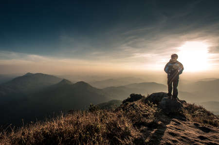 Hiker with backpack standing on top of a mountain and enjoying sunriseの写真素材