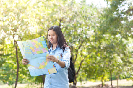 Women traveler with backpack checks map to find directions in the park of Thailand,active people...